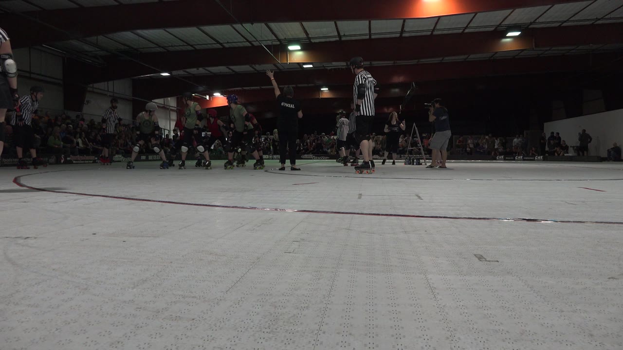 Low rink-side view of roller skaters and spectators indoors.