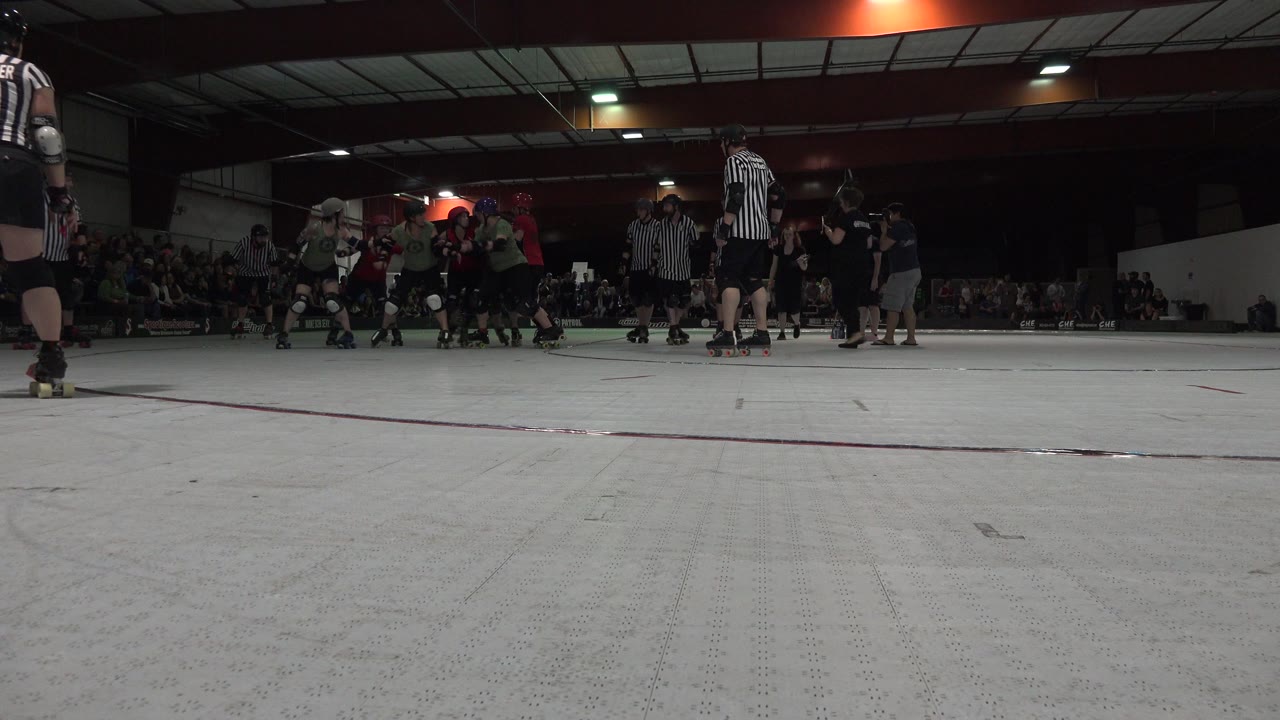 Low rink view of roller sport players and referees inside a crowded venue.