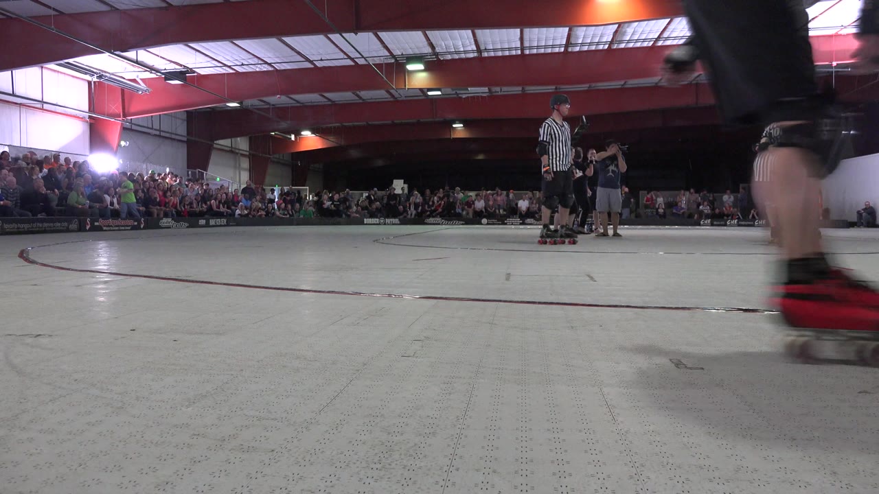 Low view across an indoor skating rink with skaters and spectators.