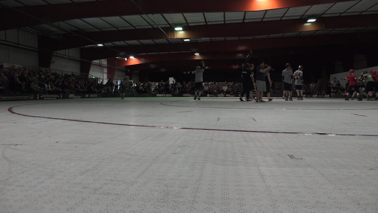 Low view across an indoor skating rink with skaters and spectators in the distance.