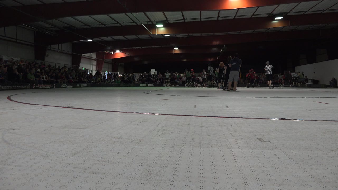 Low wide view of an indoor skating rink with skaters and spectators in the distance.
