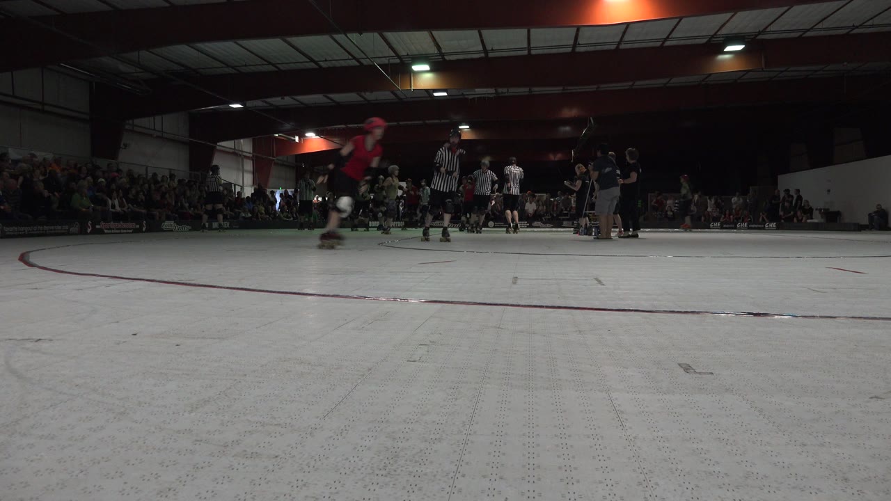 Low rink view with skaters and spectators in an indoor roller derby venue.