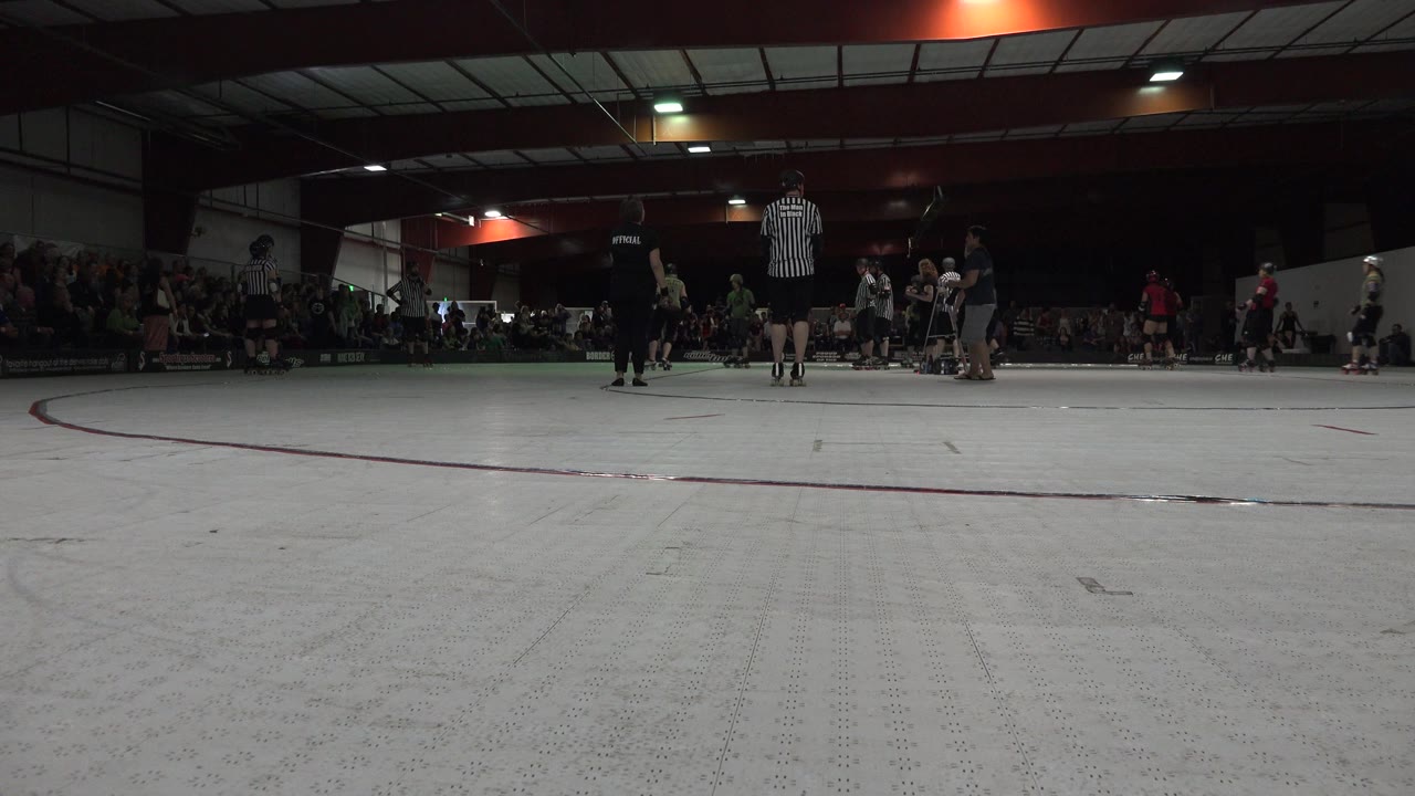 Low rink-side view in Denver shows roller skaters near a striped referee, with a seated crowd across the dim gymnasium at the start of the clip.