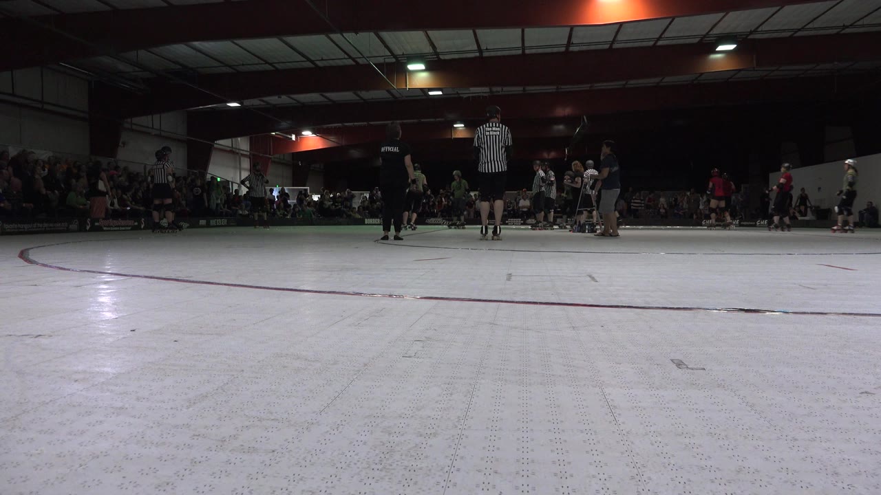 Denver gymnasium frame shows skaters clustered near center court, a referee standing upright, and spectators seated in the darker background.