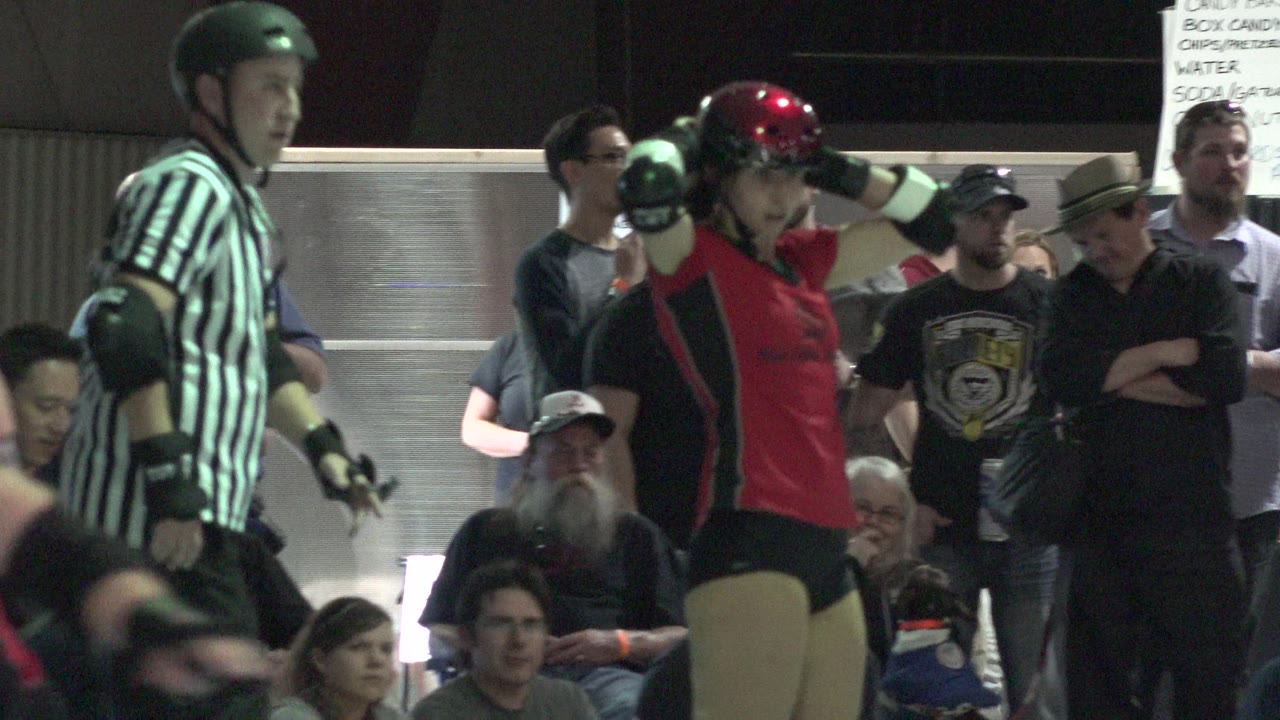 Roller derby player in red beside a striped referee near spectators.