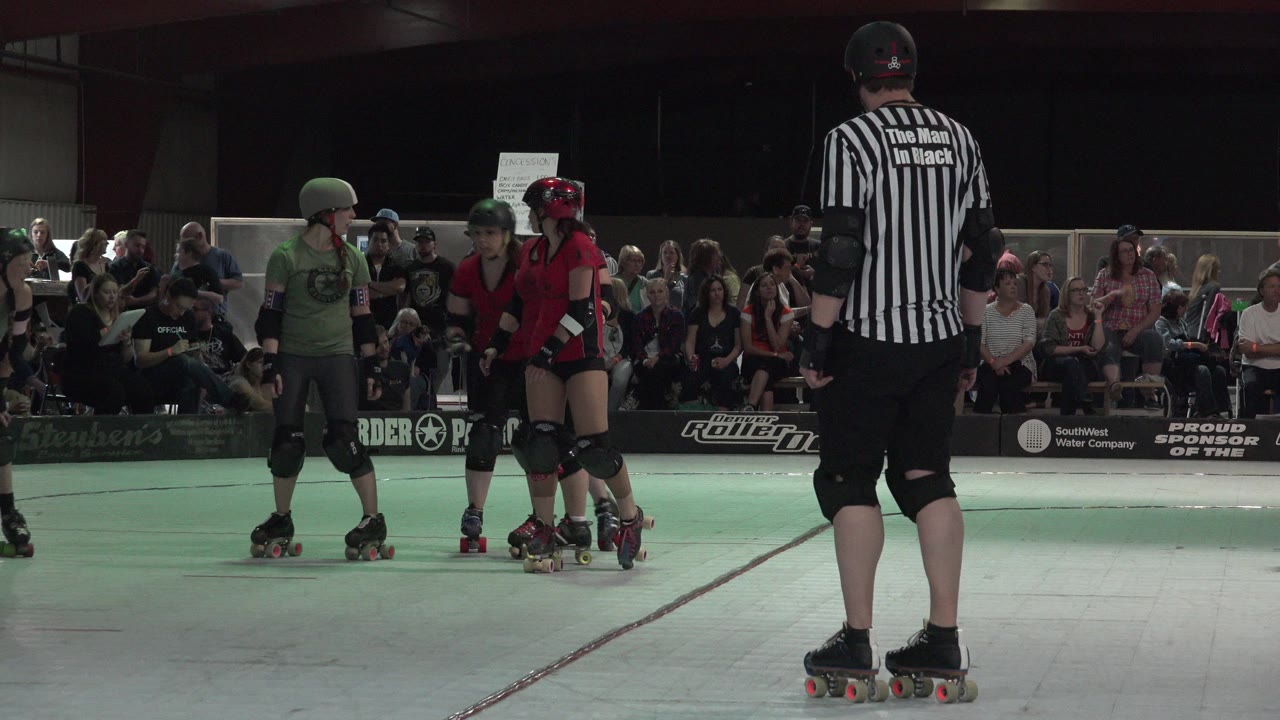 Roller derby players in green and red jerseys face each other near a referee.