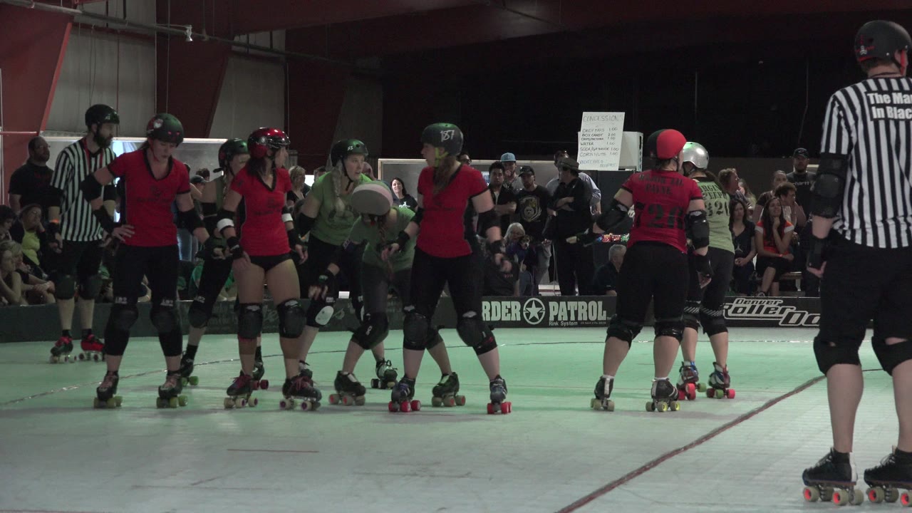 Roller derby skaters and referees on an indoor rink.