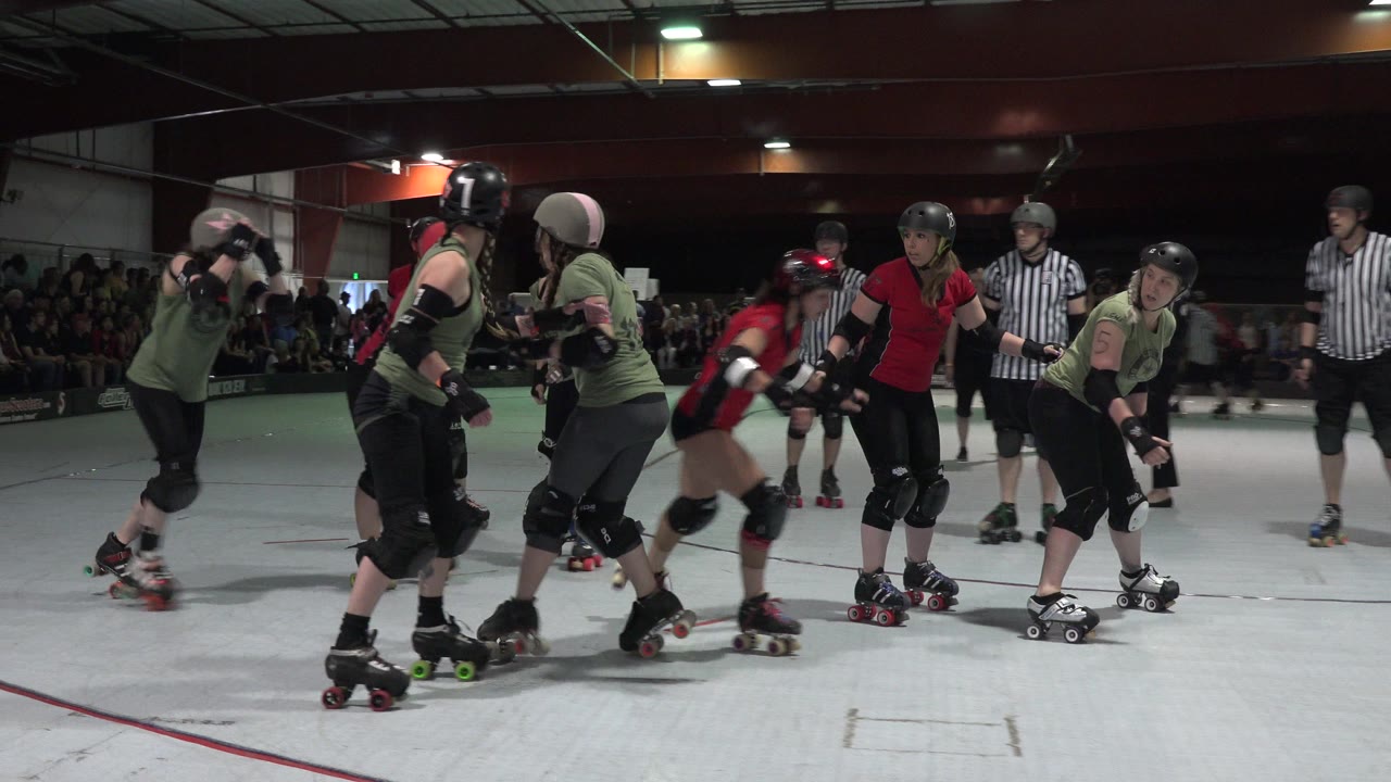 Roller derby skaters cluster on a white indoor rink.