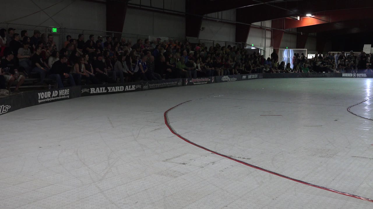 Denver roller rink frame with open skating floor, a red curved line in the foreground, a crowd seated along the far boards, and bright light near a doorway in the background.