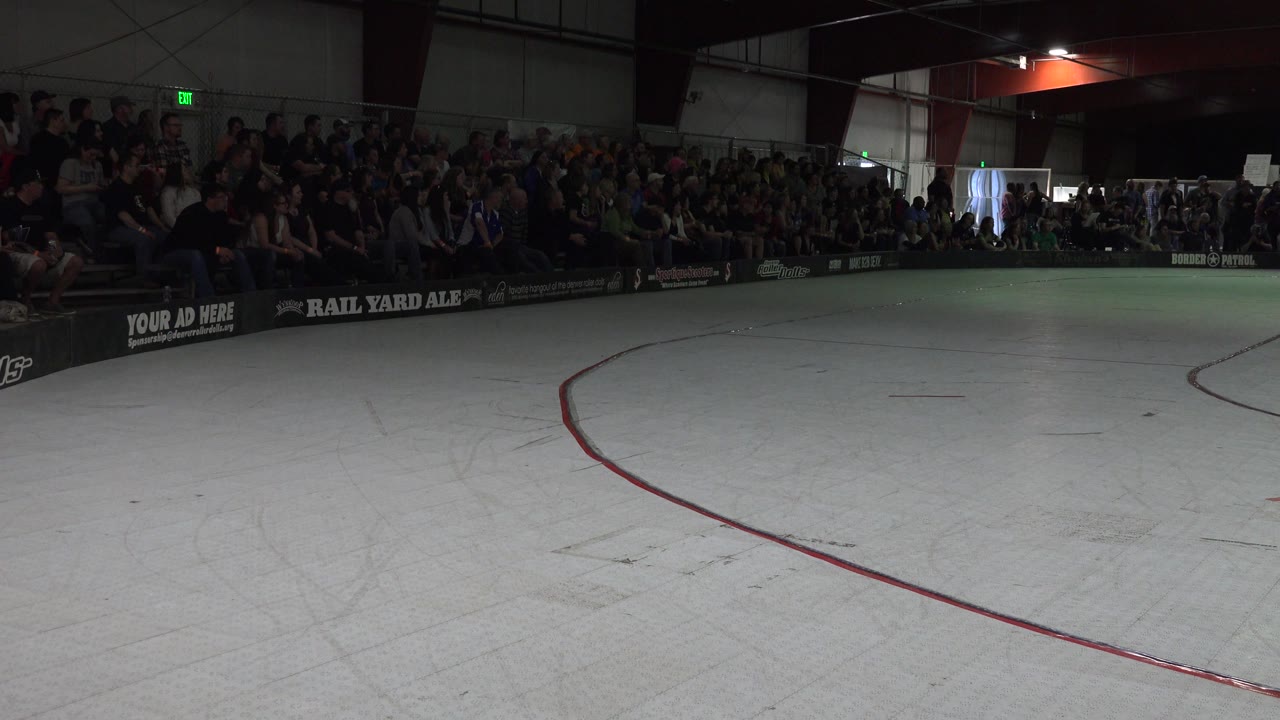 Indoor rink with empty foreground, curved red marking, and crowded bleachers.