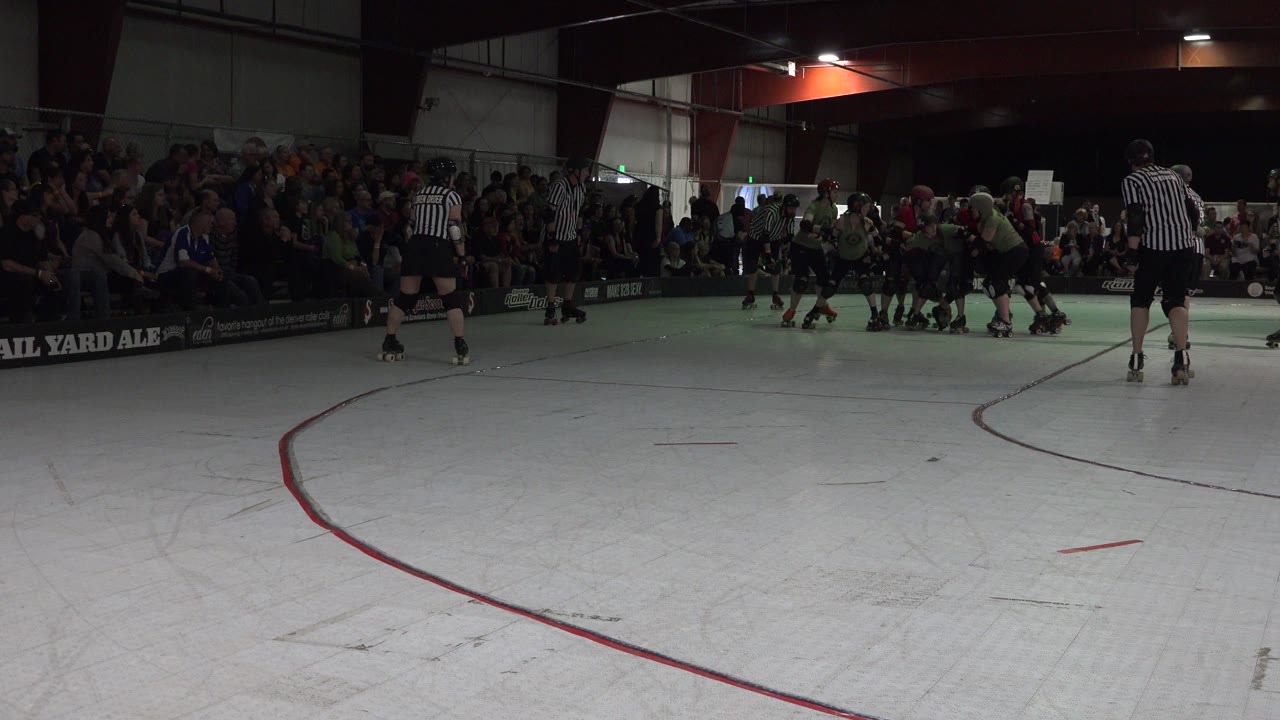 Indoor rink with skaters, referees, and spectators.