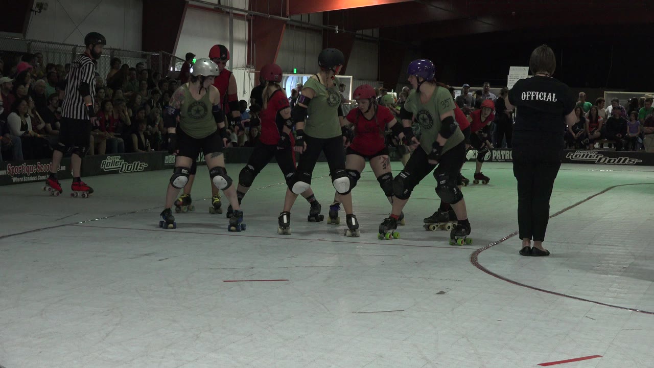 Roller skaters in red and green line up on an indoor rink.