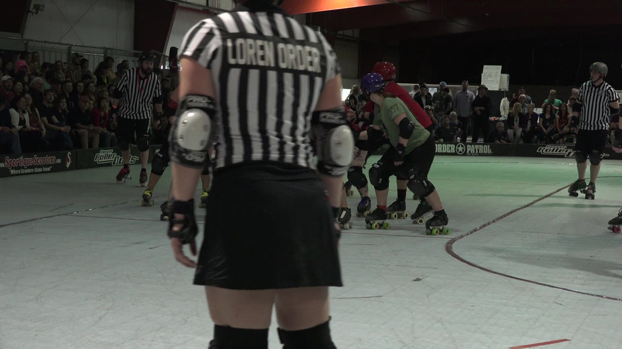 Roller derby referee in foreground with skaters on an indoor rink