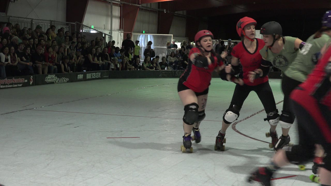 Roller derby skaters make contact near the camera on an indoor rink.