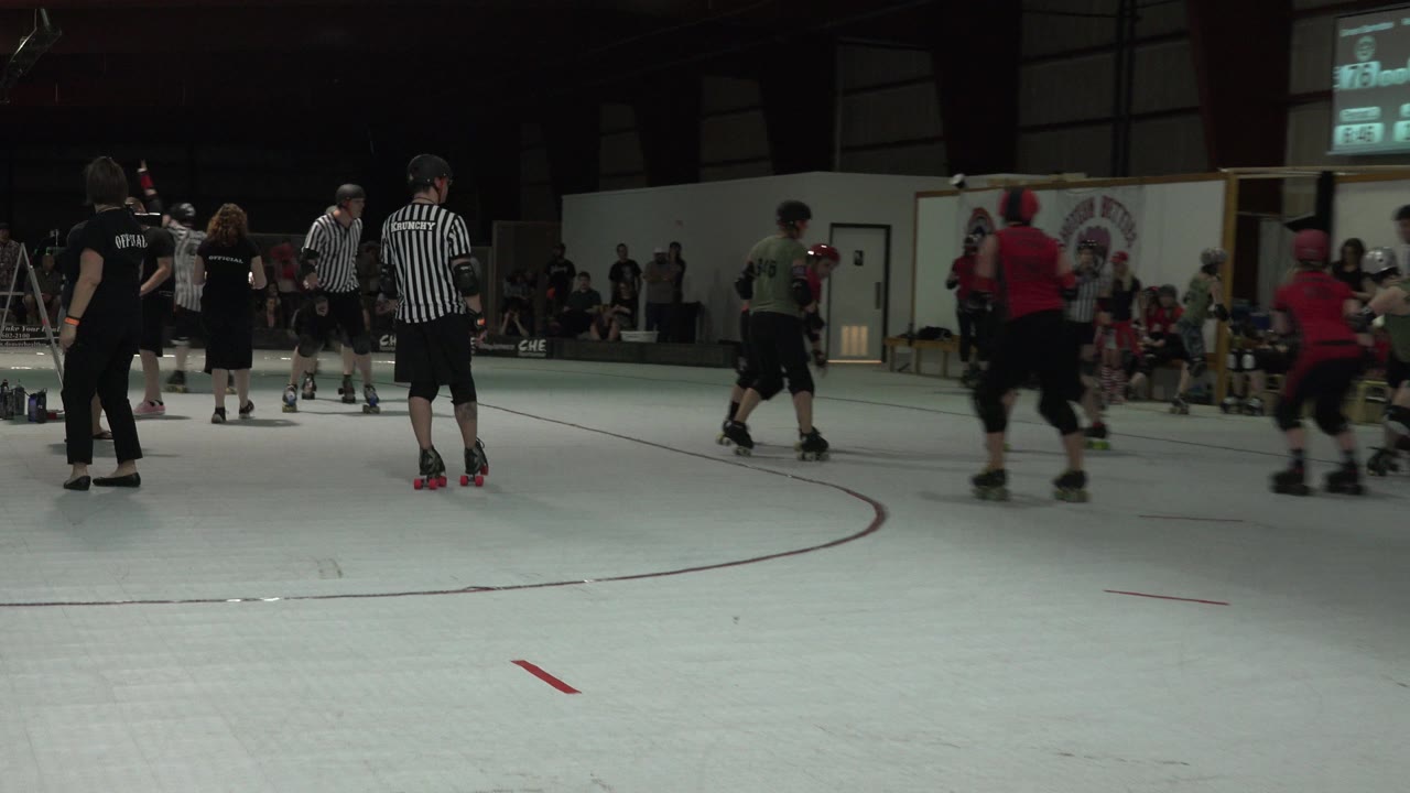 Youth hockey players in red, black, and white uniforms move across the midground as referees stand near the center of the indoor Denver rink.