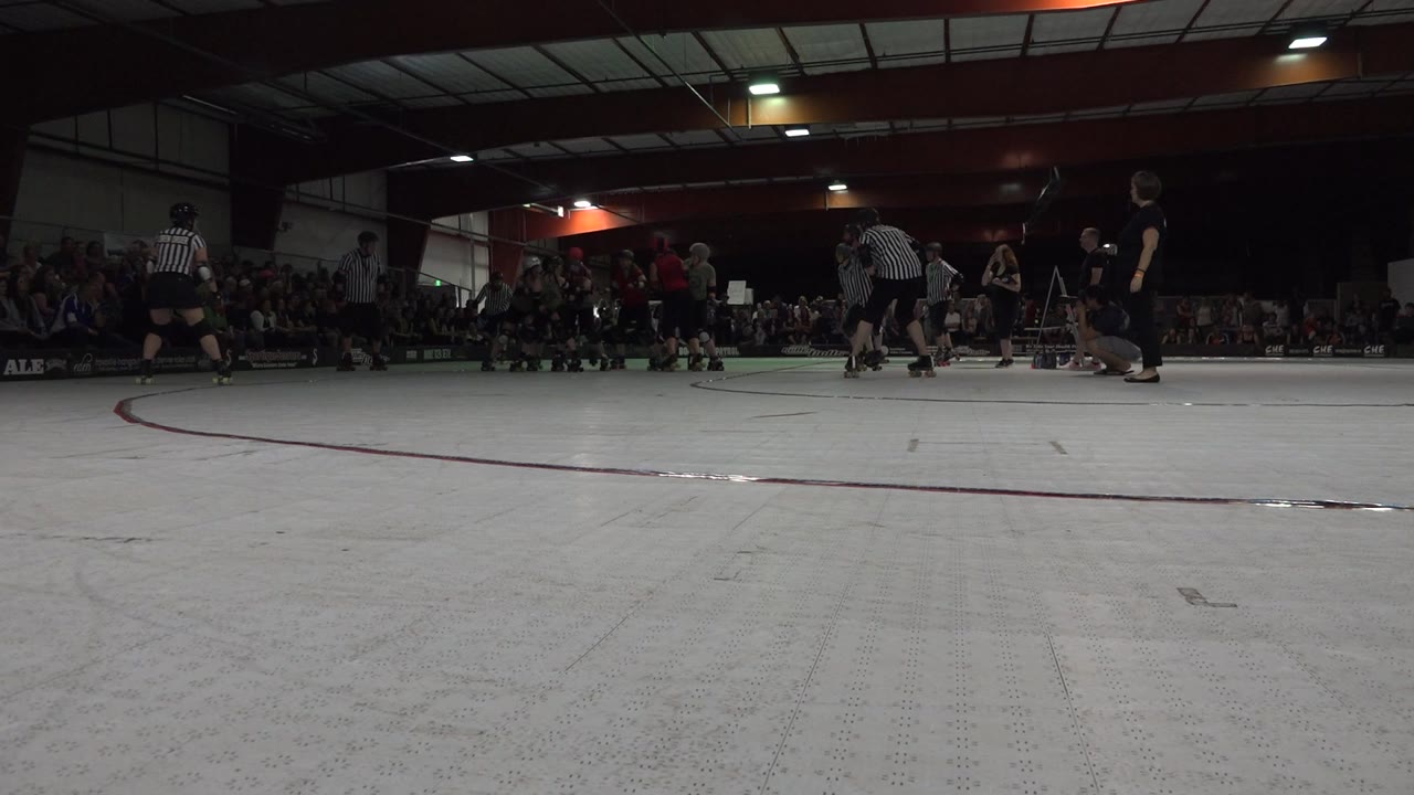 Low-angle indoor rink with skaters, referees, and spectators.