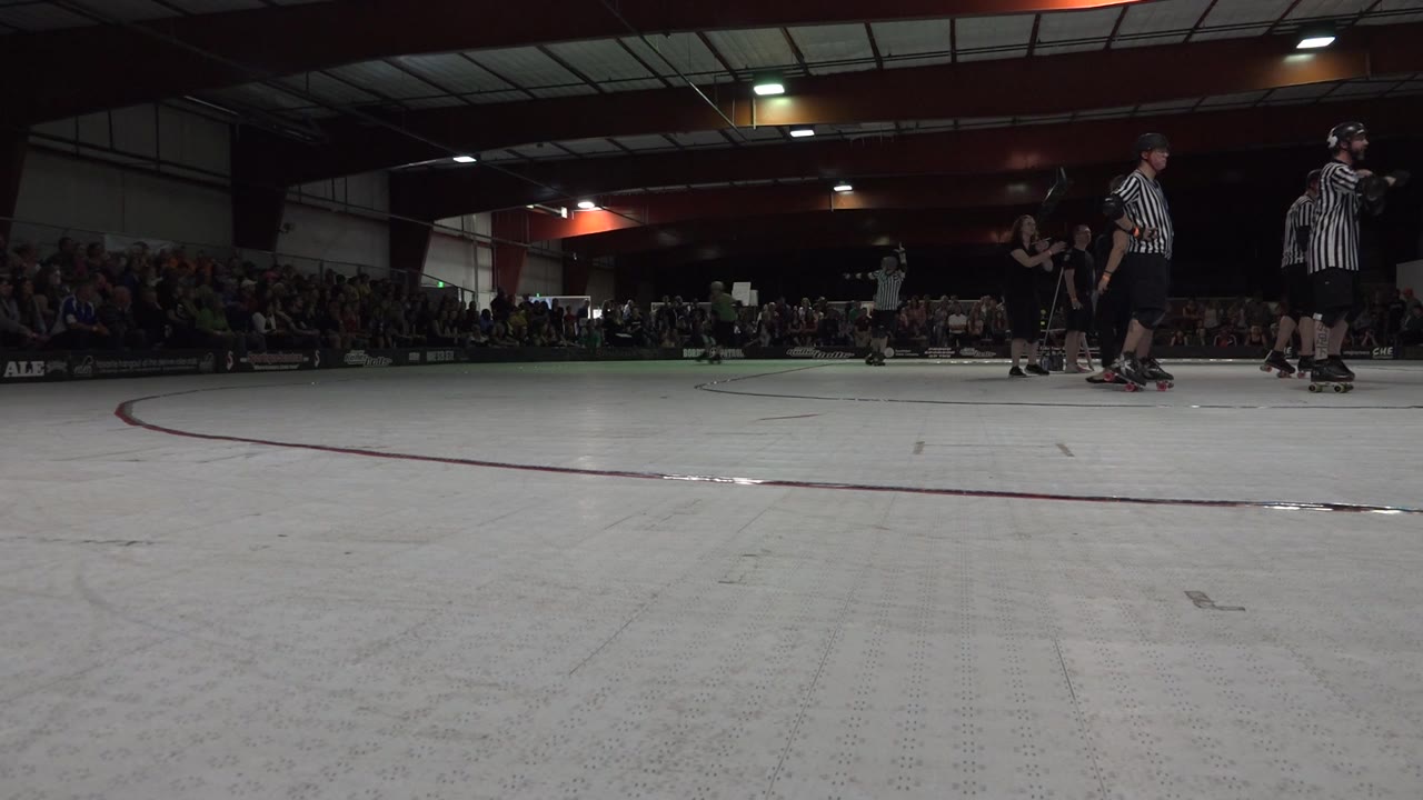 Referees and skaters remain on the right while a skater appears farther back on the rink.