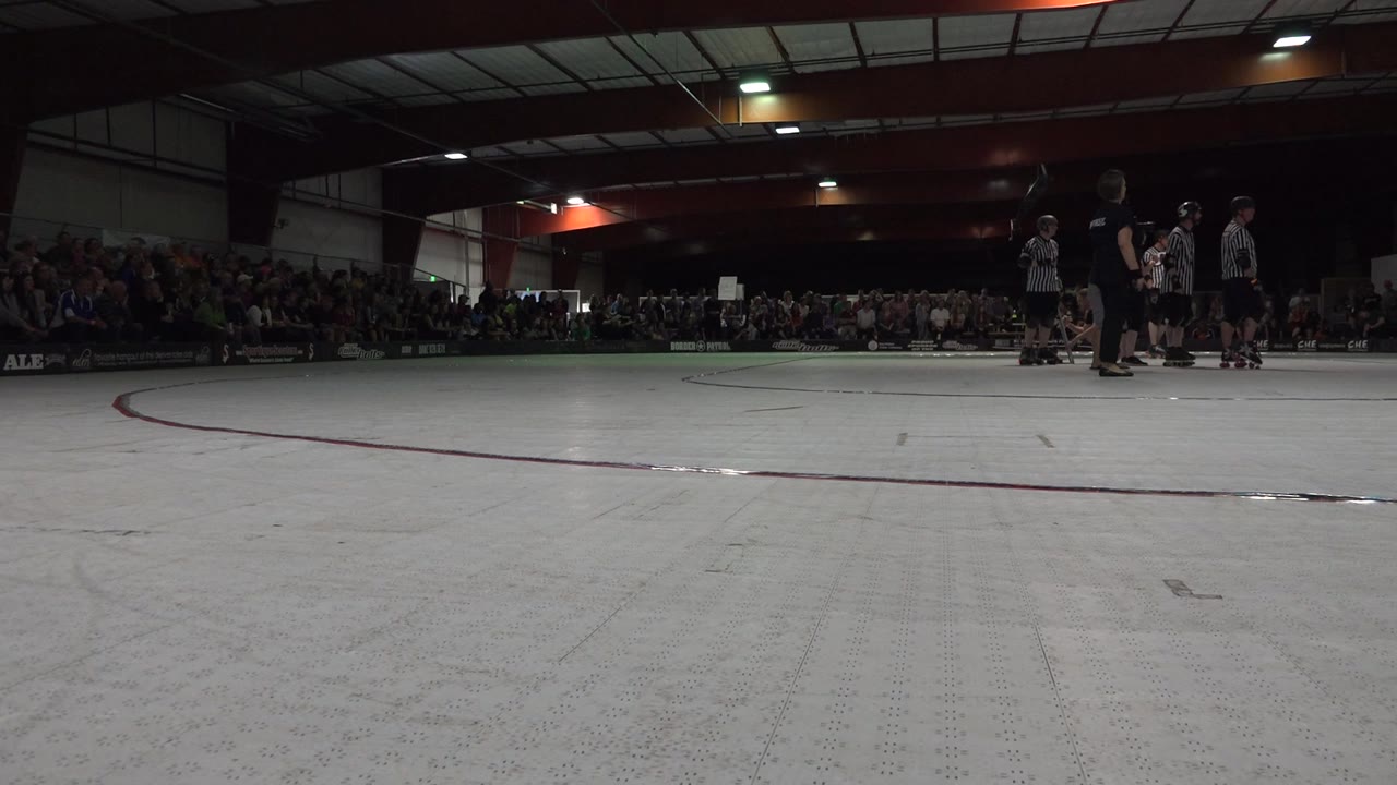 Low view across an indoor roller rink toward skaters and spectators.