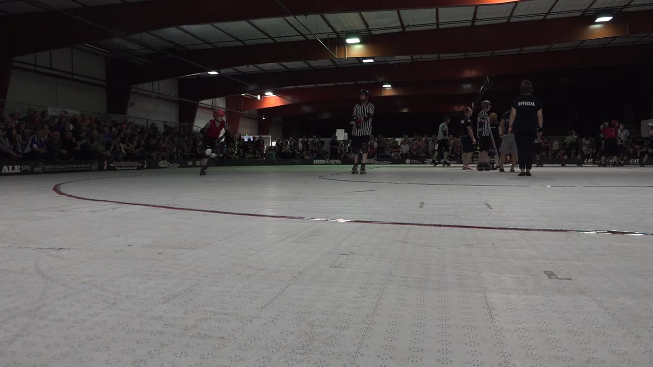 Indoor rink with a child in red near officials and a crowd.