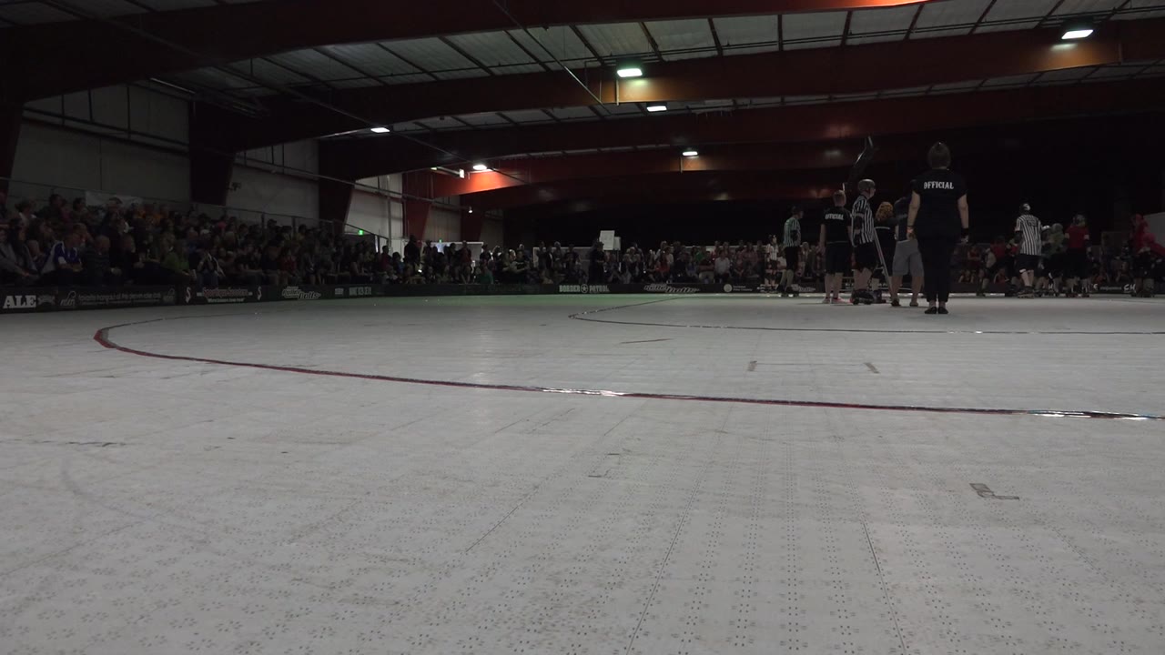 The Denver rink remains framed from floor level as a small group of skaters stands near the far boundary with spectators filling the background benches.
