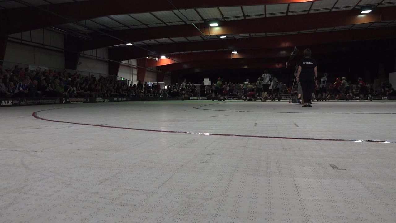 At 0:01, the Denver rink floor remains open in front while a cluster of skaters and an official stand near the far side in front of the crowd.