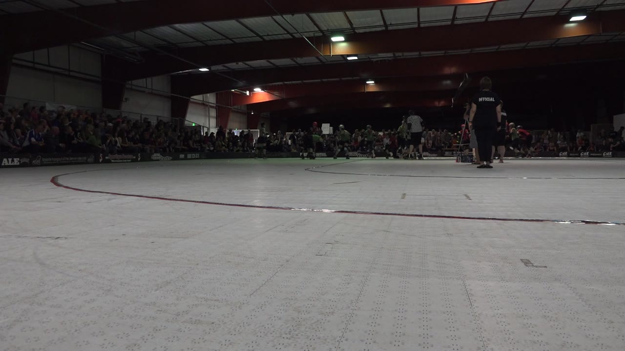 Indoor skating competition with officials on the right and spectators behind the rink.