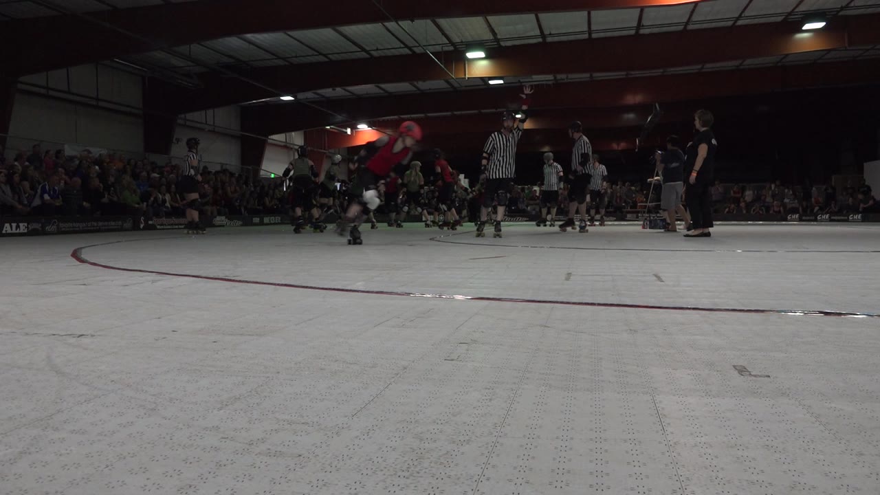 Low-angle indoor roller rink with skaters and spectators.