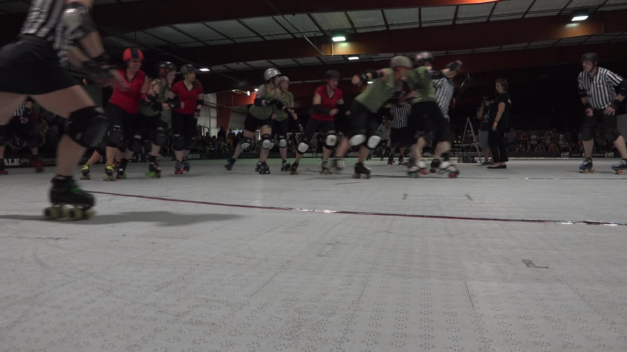 Roller derby skaters move across the rink as a referee passes close to camera.