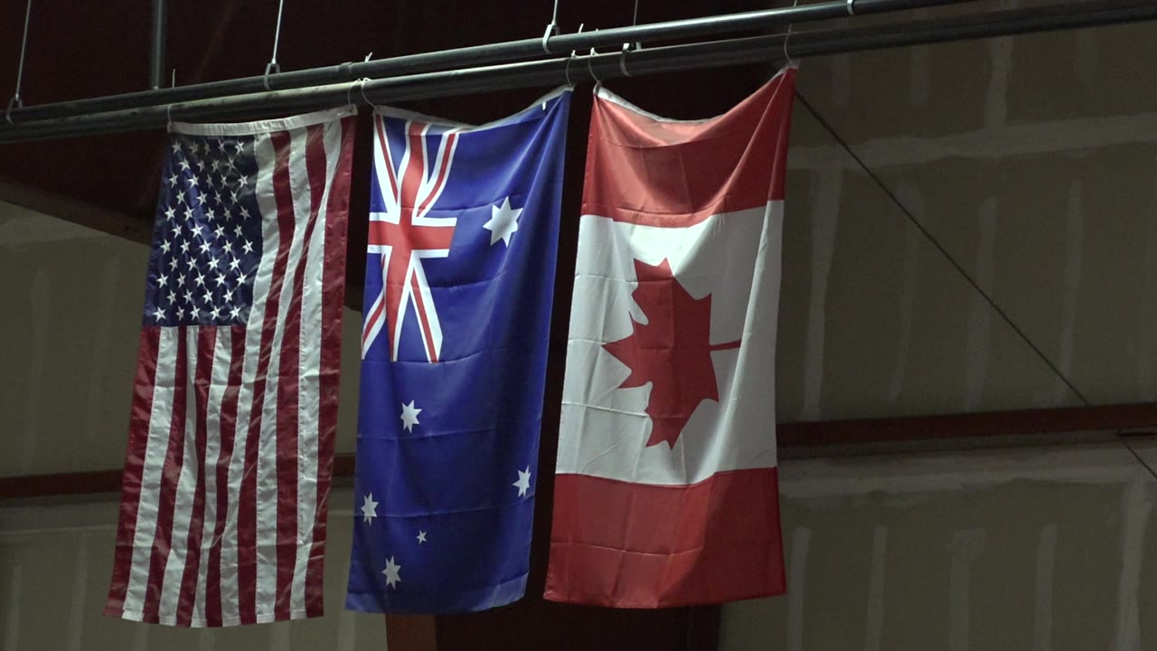 Three vertical national flags for the United States, Australia, and Canada hang from a metal bar in Denver, Colorado, with no visible people.