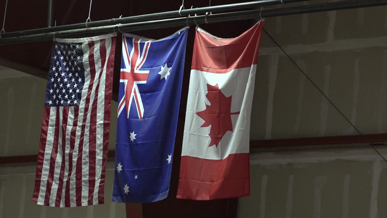 Three flags on a pipe with a dark stage wall behind them.
