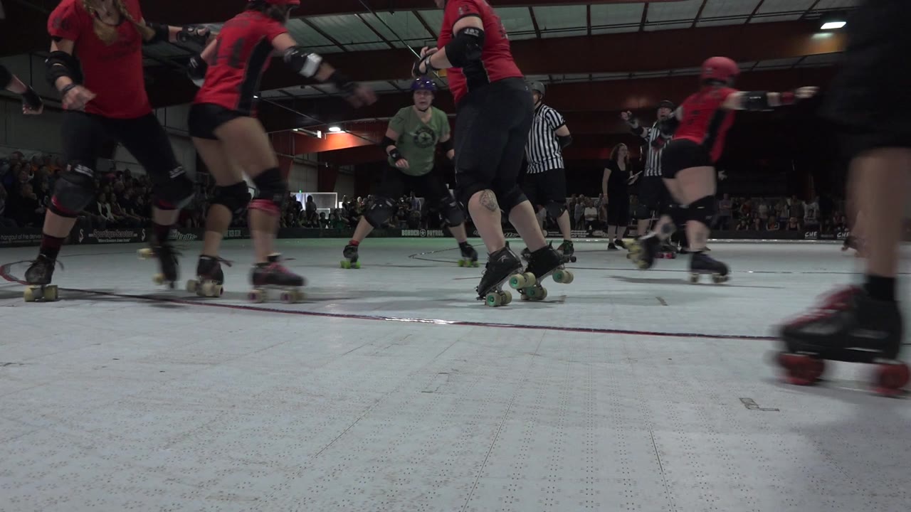 Roller derby pack moves past the camera with a referee behind.