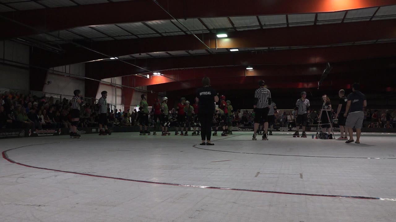 Low view across an indoor rink with players, referees, and spectators.