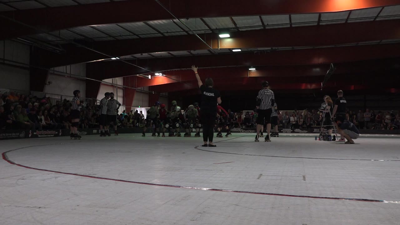 A Denver indoor rink scene shows youth hockey players in green and red near center ice, referees in striped shirts, and seated spectators behind the boards.