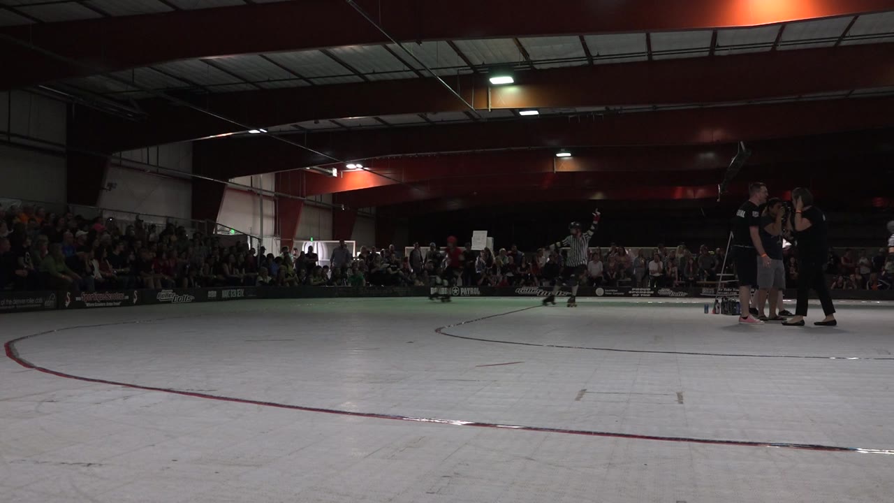 Denver roller rink scene with a referee standing near the center background, staff grouped at the right, and spectators seated along the far wall.