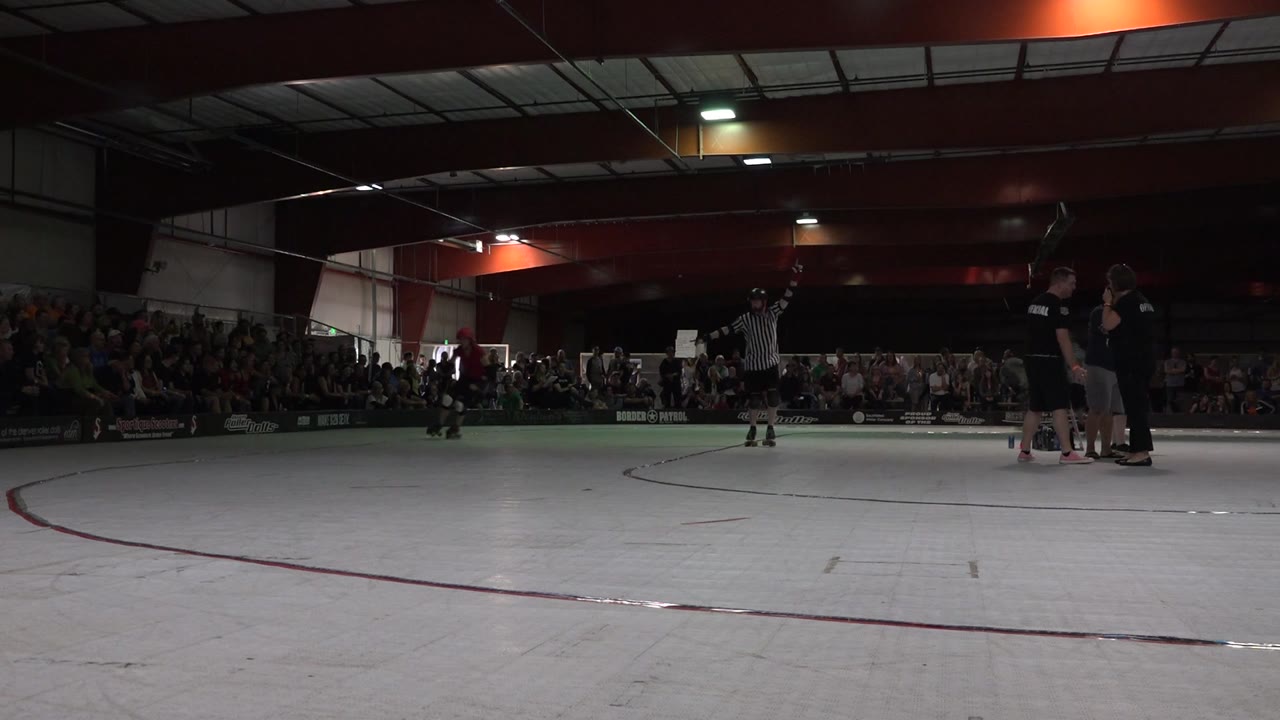 Referee signaling beside the rink while staff stand at the right.