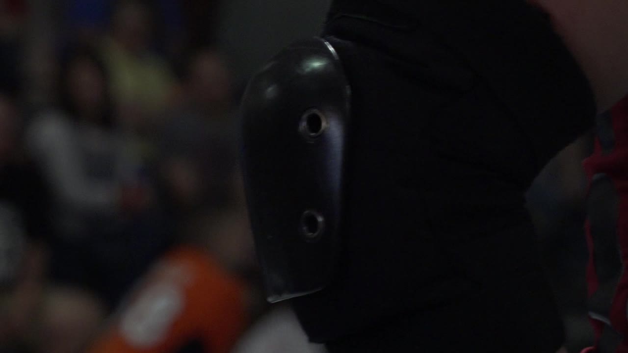 Close-up of a black elbow guard on an athlete's arm with blurred spectators behind.