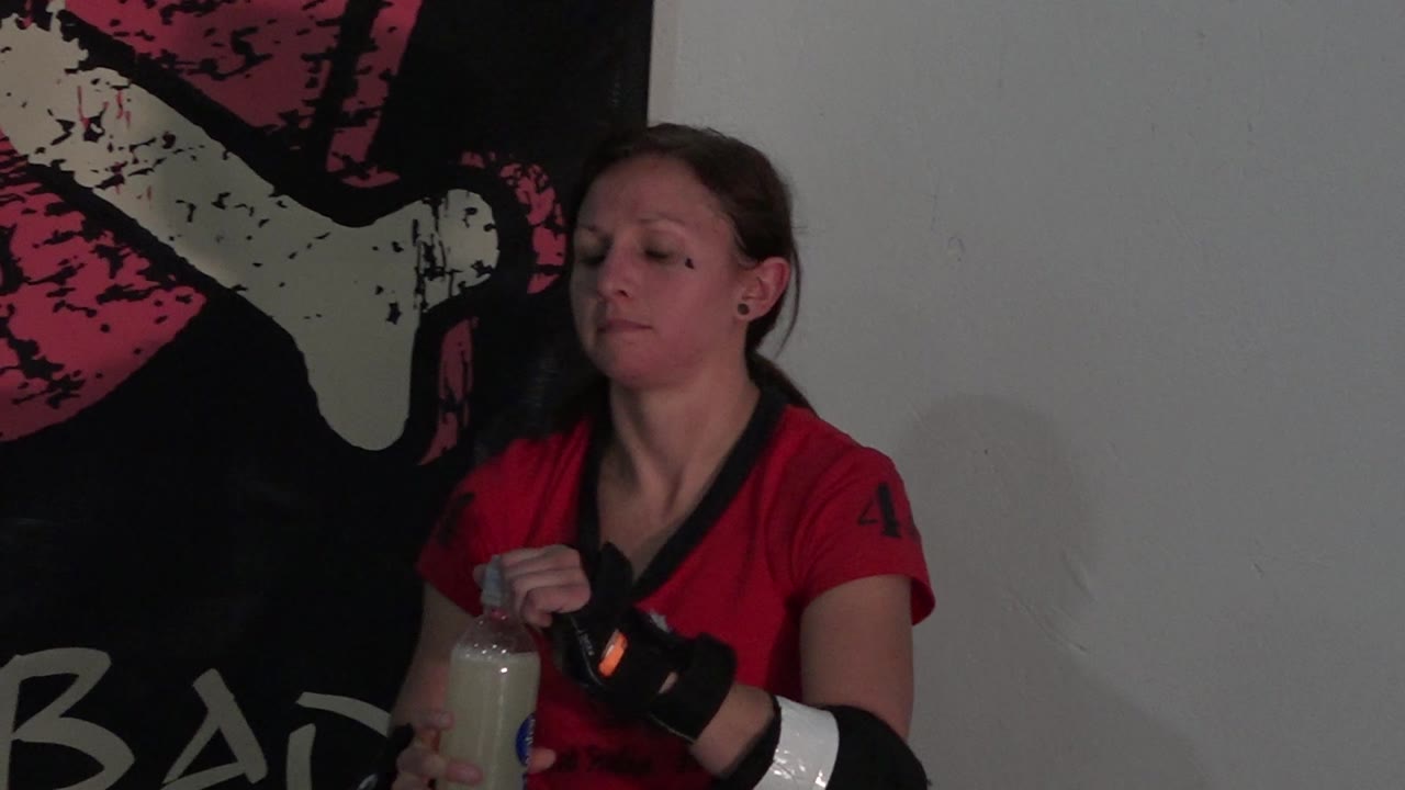 In Denver, Colorado, the seated woman keeps her gaze lowered while gripping the drink bottle, with the pink and white wall graphic partly behind her shoulder.