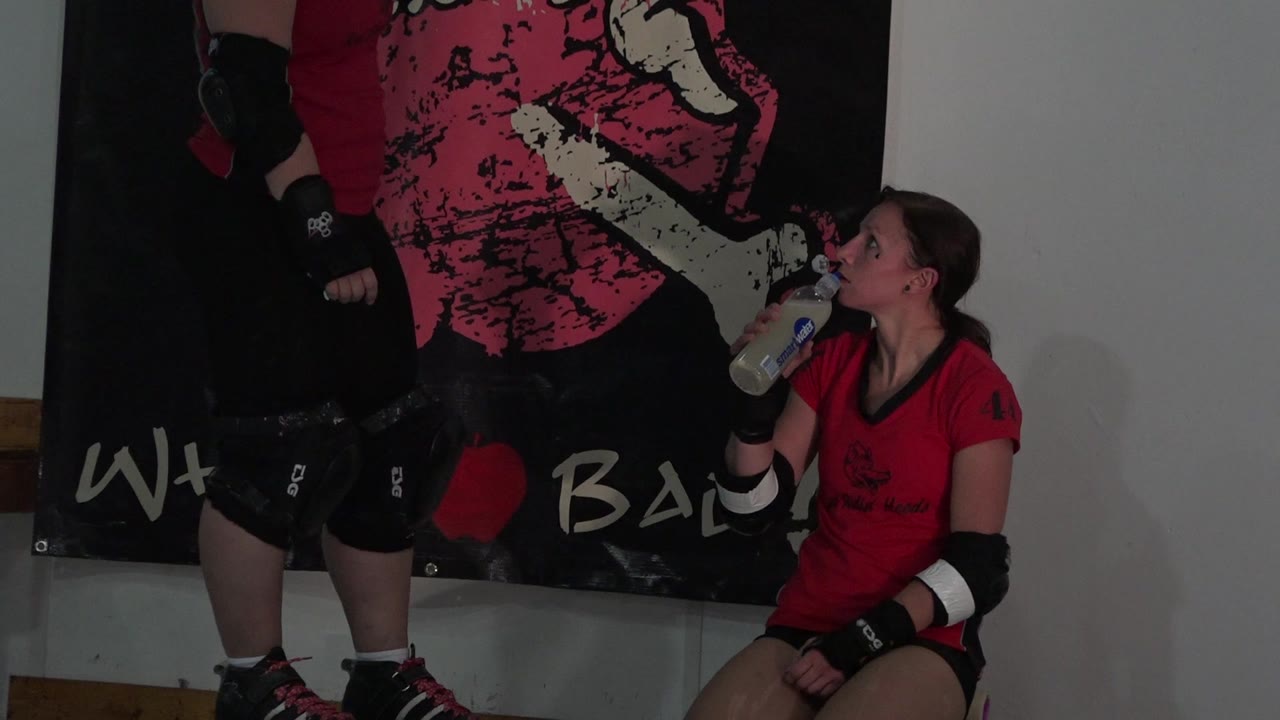 The Denver frame holds on a standing skater in helmet and pads beside a seated teammate holding a bottle, with the graphic wall banner filling the background.