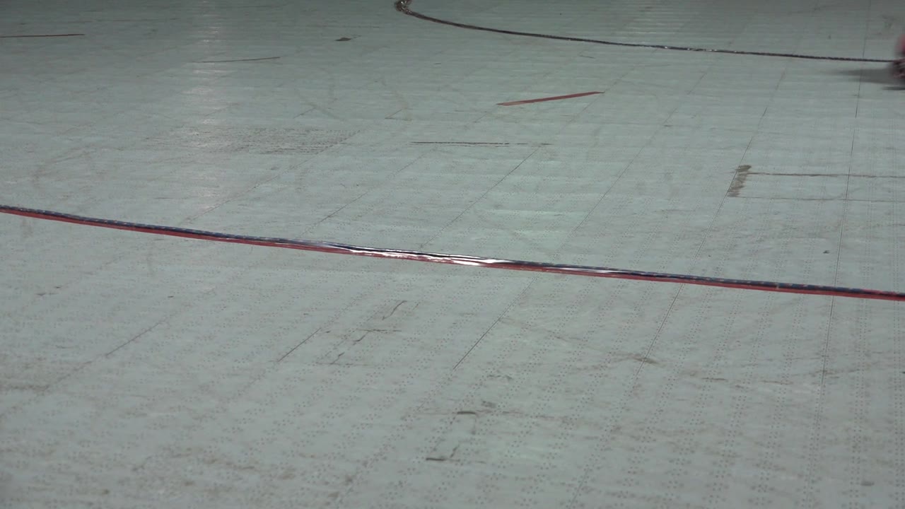 The Denver rink floor fills the frame with red curved and straight markings while several skaters are cropped at the top edge.
