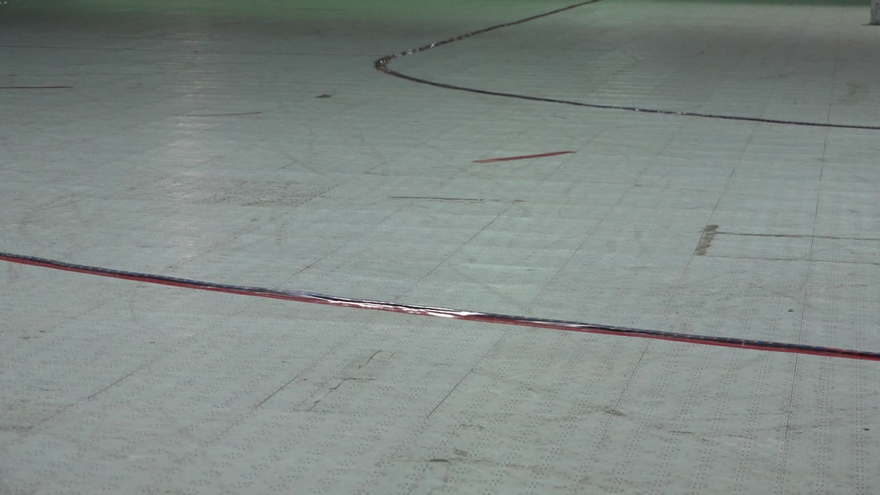 Pale roller rink floor with red and black curved markings.