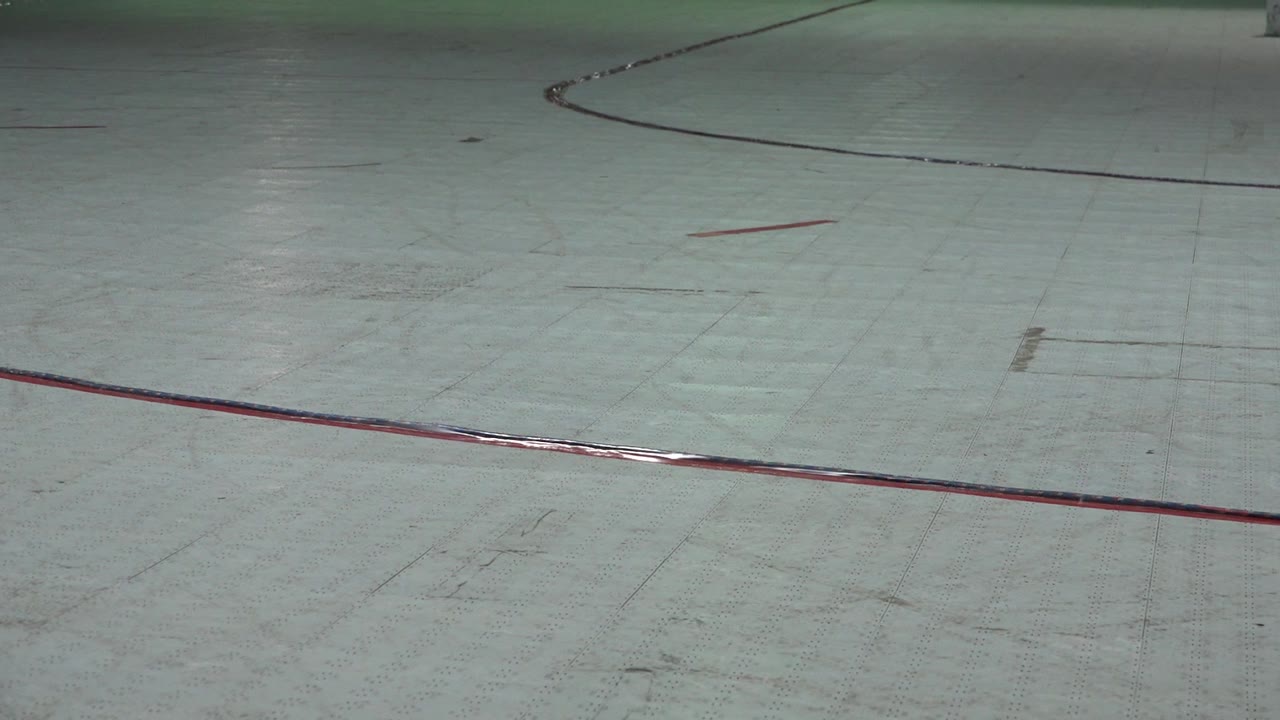 Denver roller rink floor one second in, with the red foreground stripe crossing the lower frame and a black curve running near the back, with no visible people.