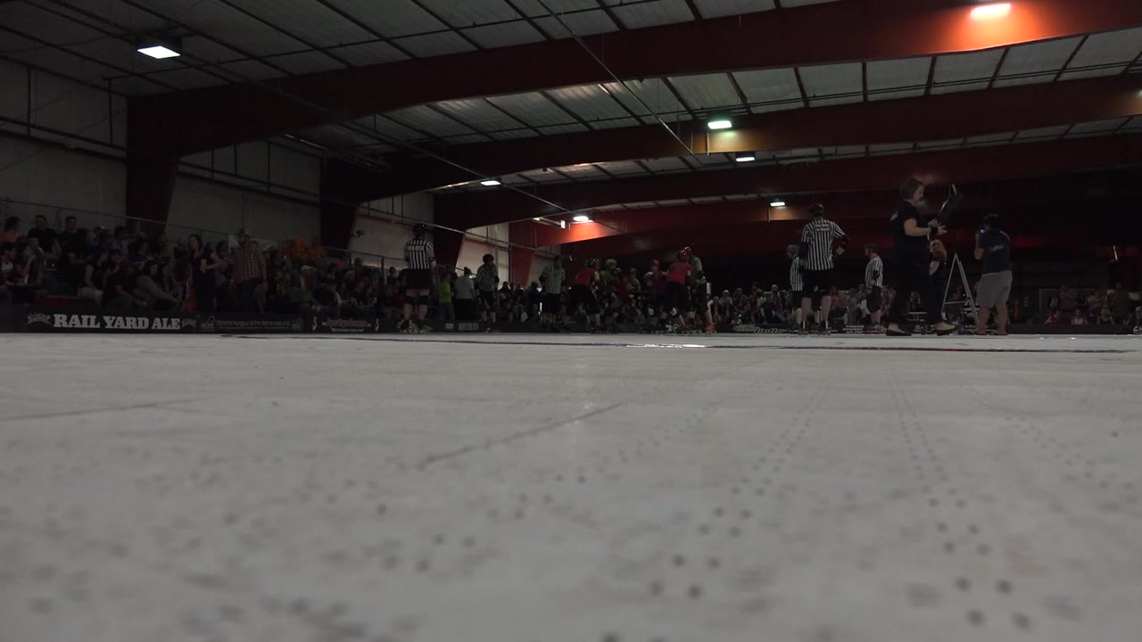 Low view across a white indoor roller rink floor with distant people near the wall.