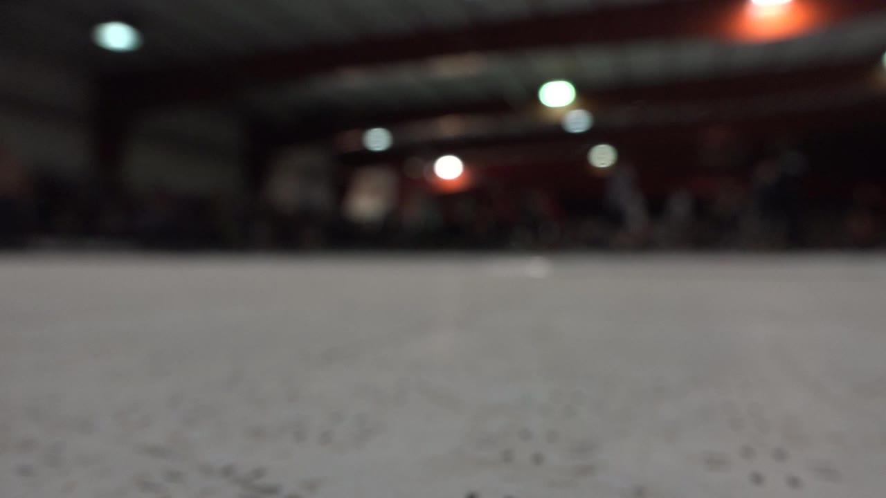Low floor-level view inside a Denver indoor roller skating rink, with the pale rink surface filling the foreground, soft overhead lights, and indistinct people in the distance.