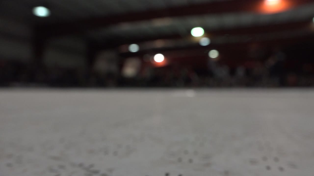 Dim roller rink with a large pale floor and blurred background figures.
