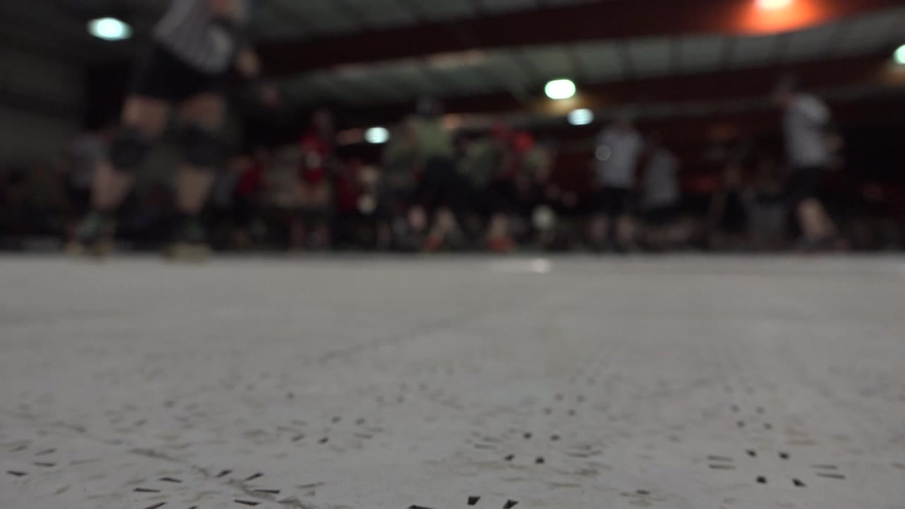 Ground-level Denver rink frame with a broad scuffed floor foreground, distant players in helmets, seated spectators, and bright ceiling lights.