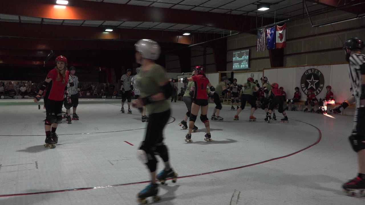 Roller derby skaters and referees on an indoor flat track.