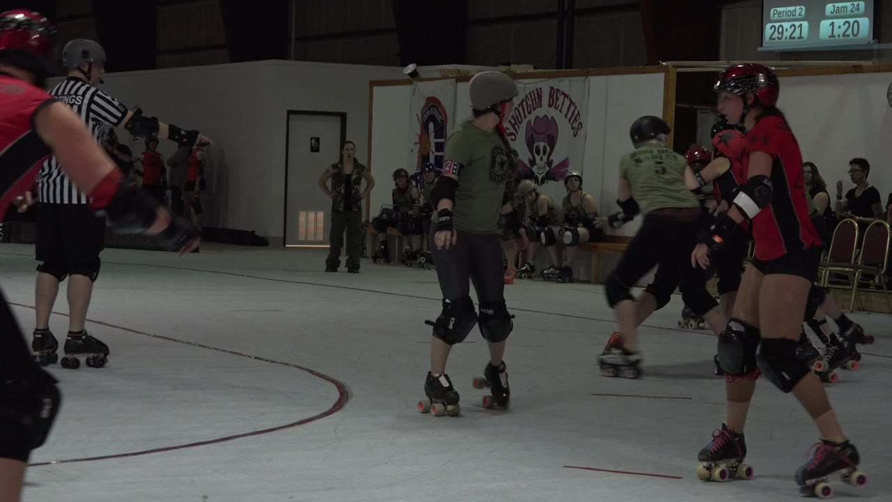 Roller derby skaters and a referee on an indoor rink.