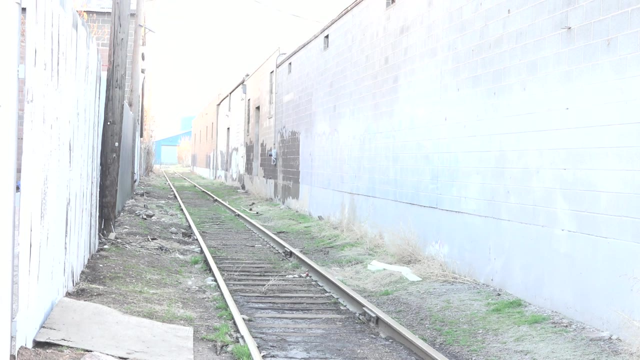 The rail line continues through the Denver corridor, with a pale wall filling the right side and track debris visible near the left edge.