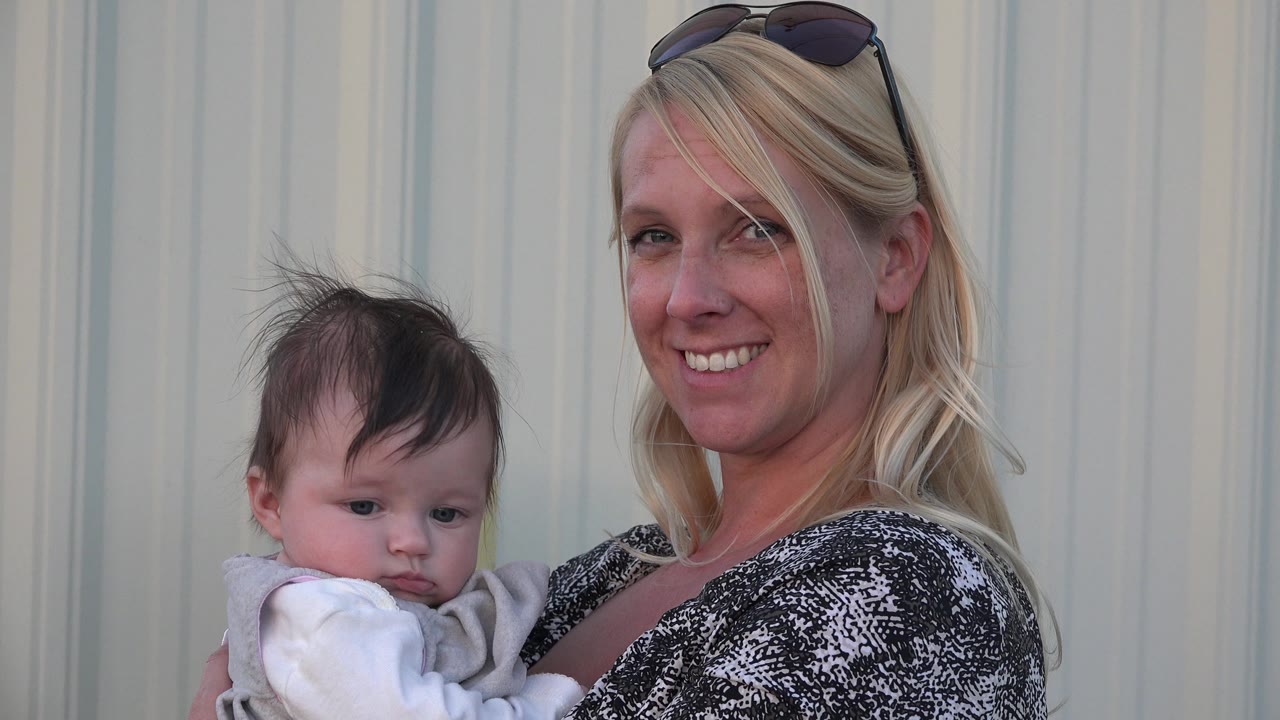In Denver, Colorado, the smiling mother holds the baby slightly lower in frame, with both faces visible near the pale ribbed wall.