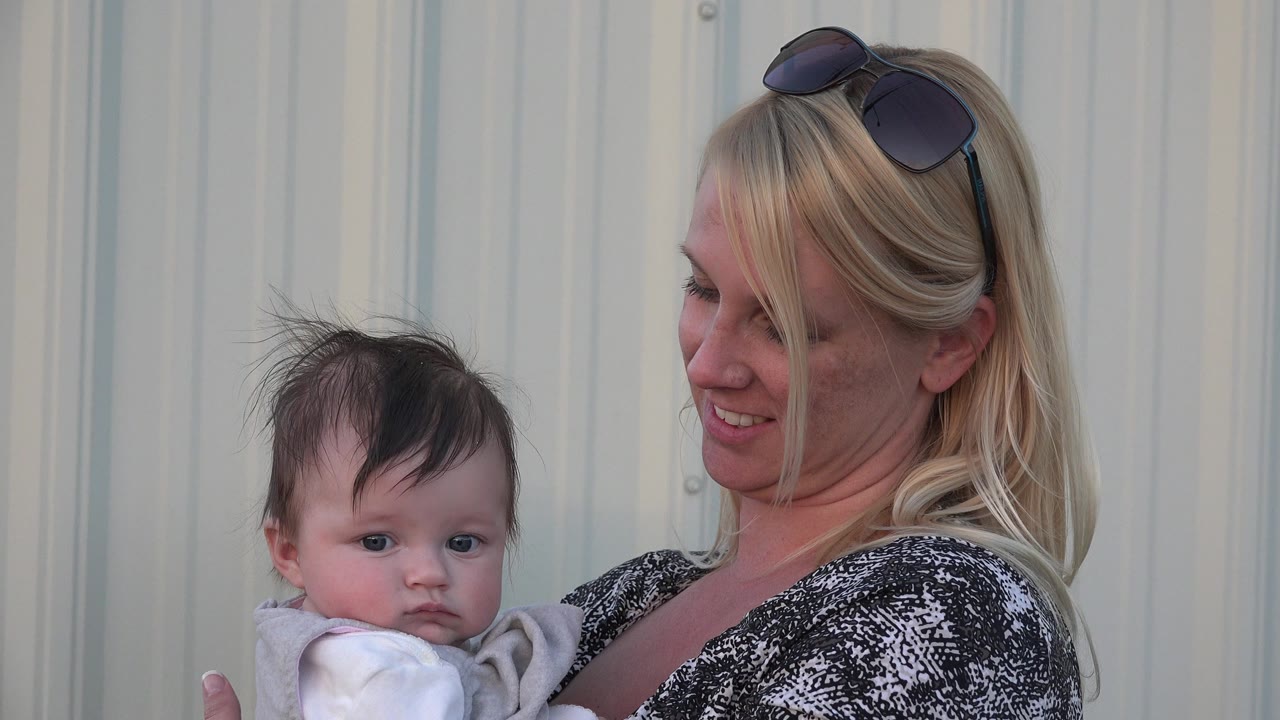 Woman holding a baby beside a light corrugated wall.